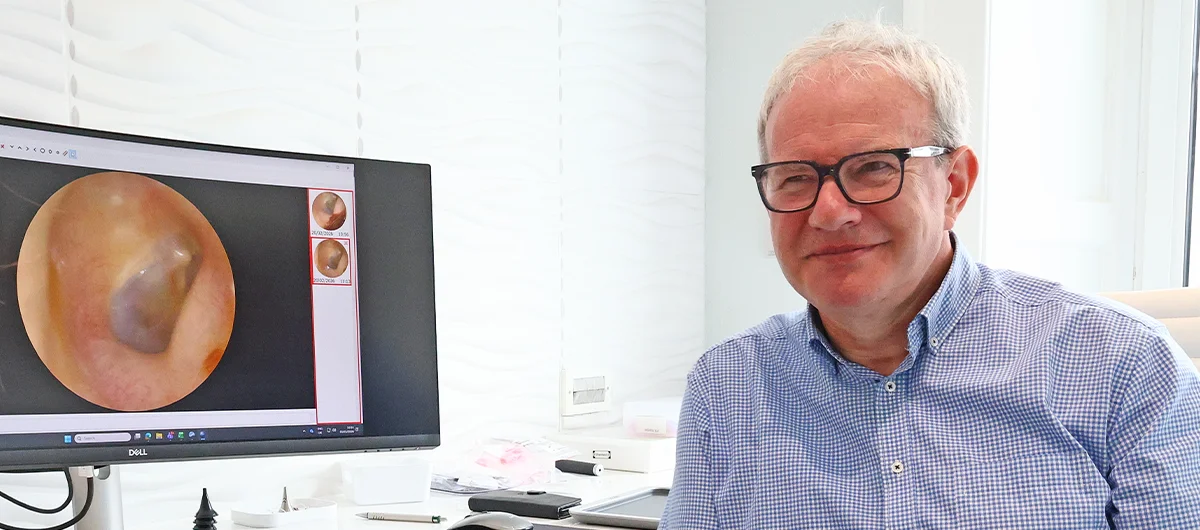 Stephen Fairfield, founder and principal audiologist at Fairfield Hearing Edinburgh, beside a video otoscopy image of an ear canal.